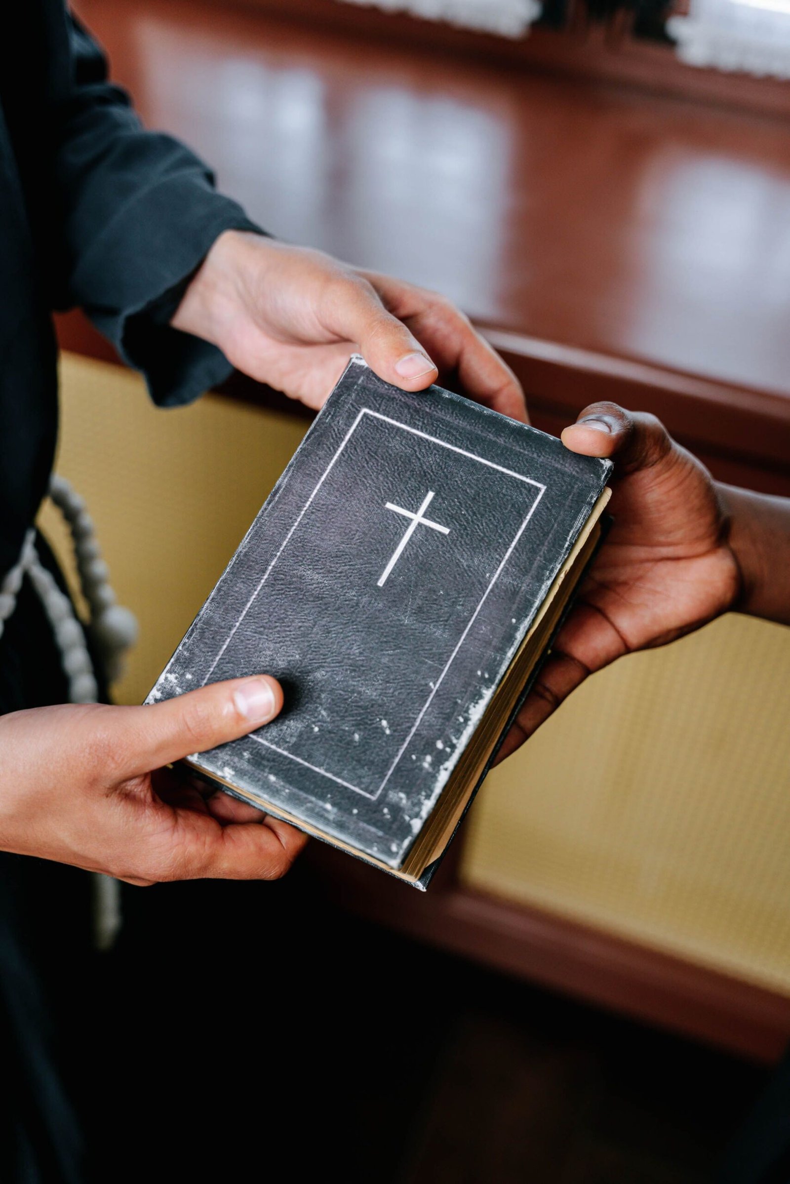 Hands exchanging a holy bible indoors, symbolizing unity and spirituality.