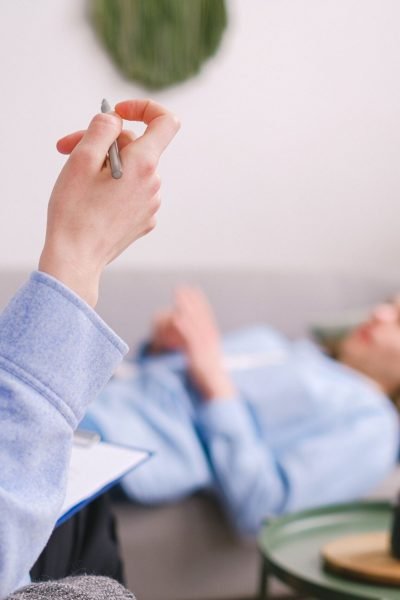 Therapist taking notes during a therapy session with a relaxed client lying on a couch.